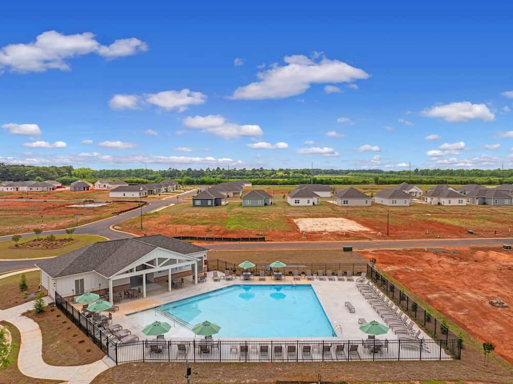 A large swimming pool surrounded by a fence with a building and a lawn in the background.