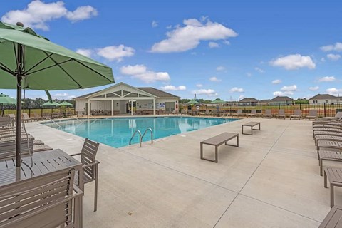 A pool area with a green umbrella and lounge chairs.