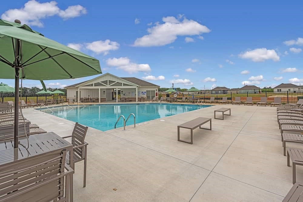 A pool area with a green umbrella and lounge chairs.