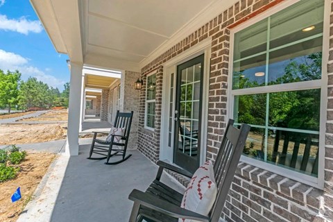 the front porch of a brick house with rocking chairs