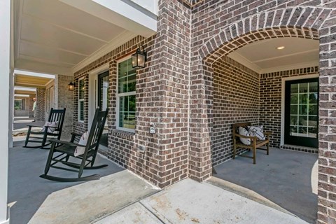 the front porch of a brick house with rocking chairs