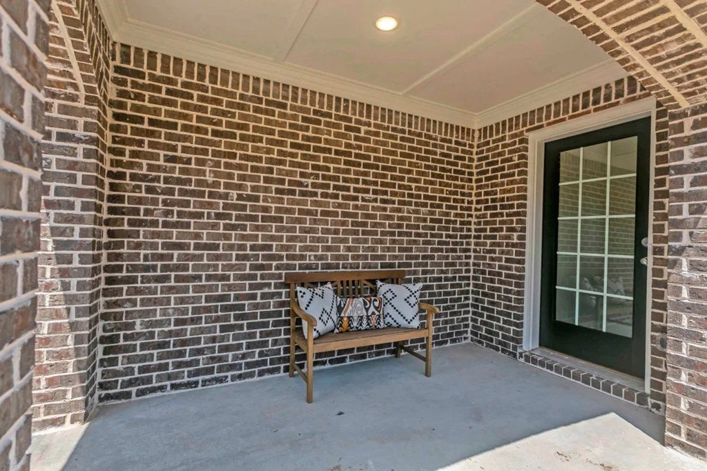 A wooden bench with a cushion sits in front of a brick wall and a glass door.