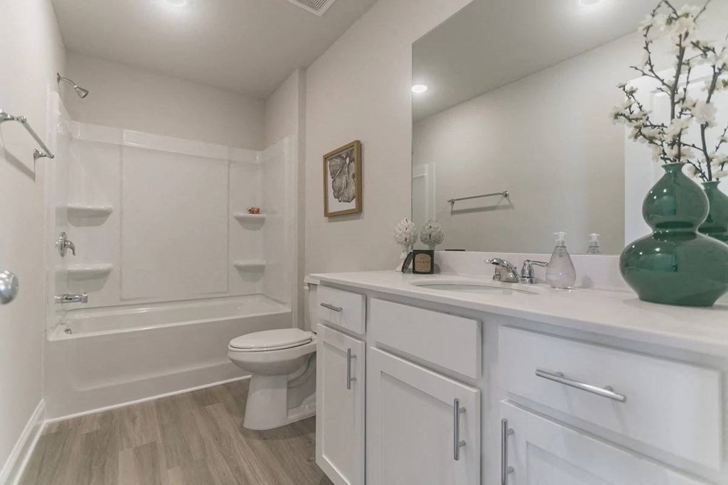A white bathroom with a green vase on the counter.