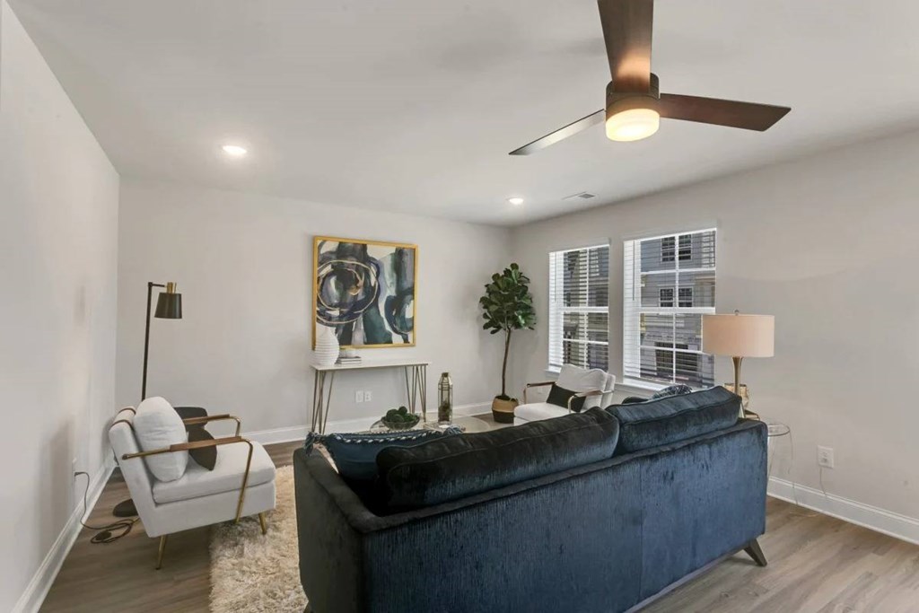 A living room with a blue couch, a white chair, and a ceiling fan.
