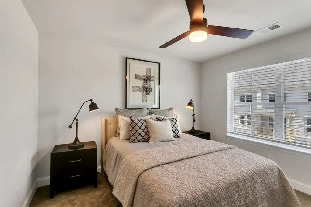 A bedroom with a bed, two lamps, and a ceiling fan.