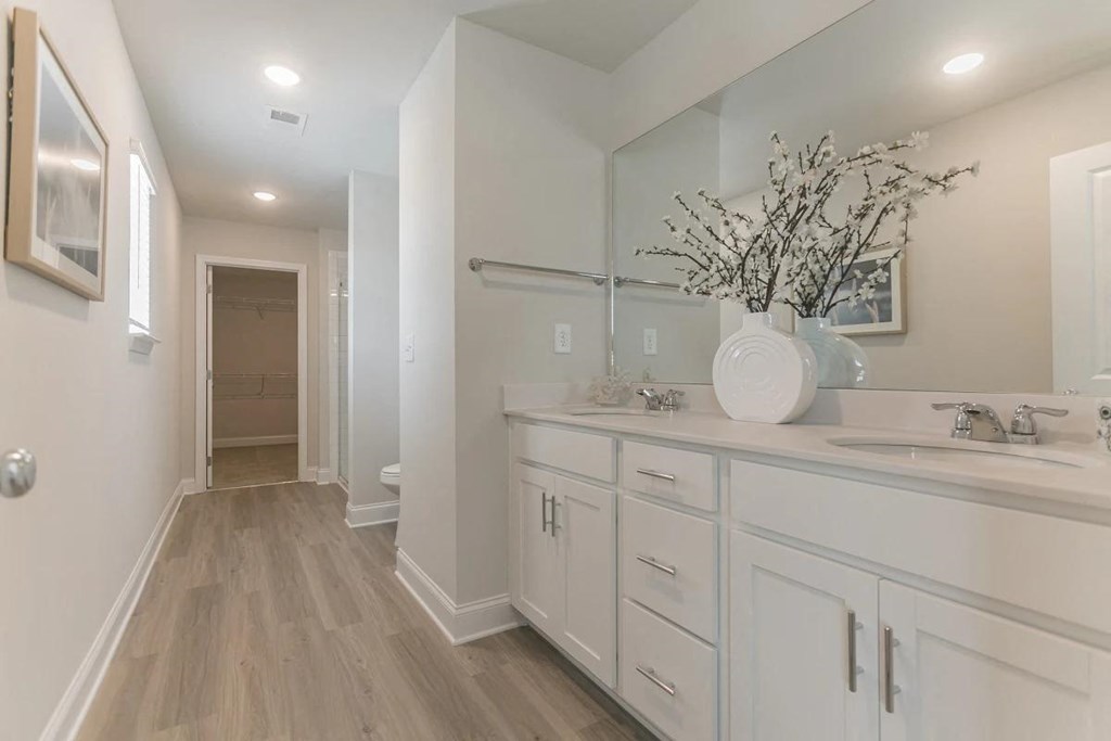 A long white bathroom with a vanity and a vase of branches on the counter.