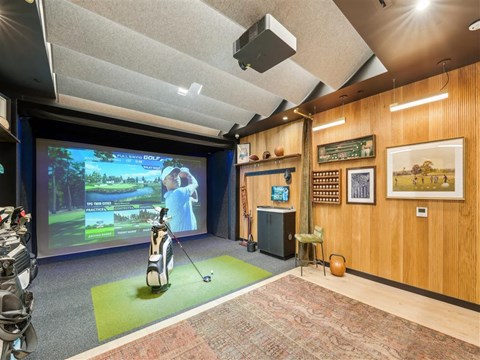 A room with a golf simulator and a TV screen showing a golf game.