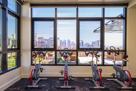 A gym with exercise bikes and a view of the city outside the window.