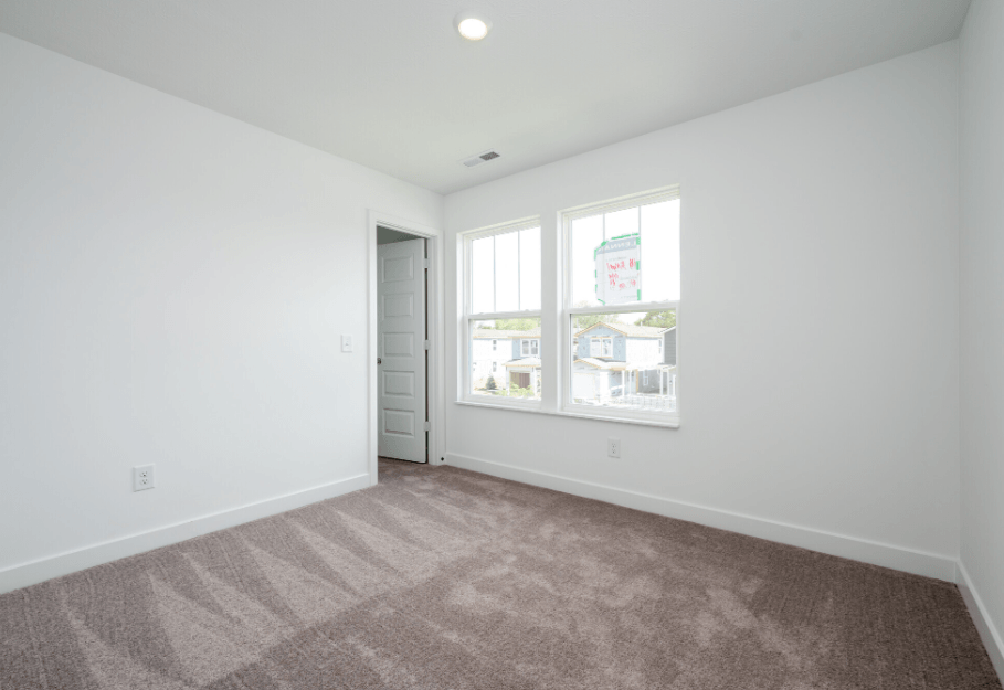 A room with a carpeted floor and a window showing a view of buildings outside.