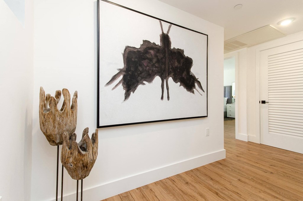 A painting of a bat hanging on a wall next to two sculptures on stands.
