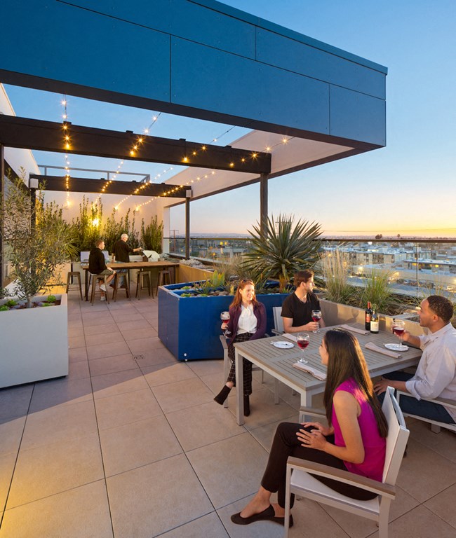 A group of people are sitting around a table on a rooftop patio.