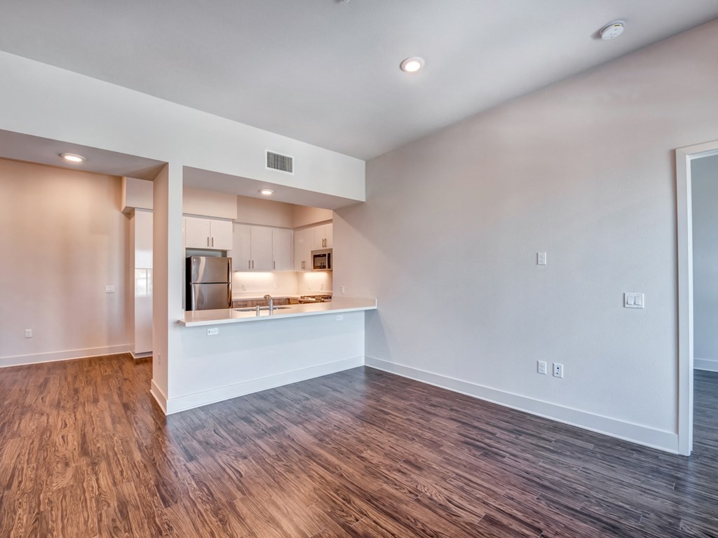 A kitchen with a refrigerator, oven, and sink is visible through a doorway.