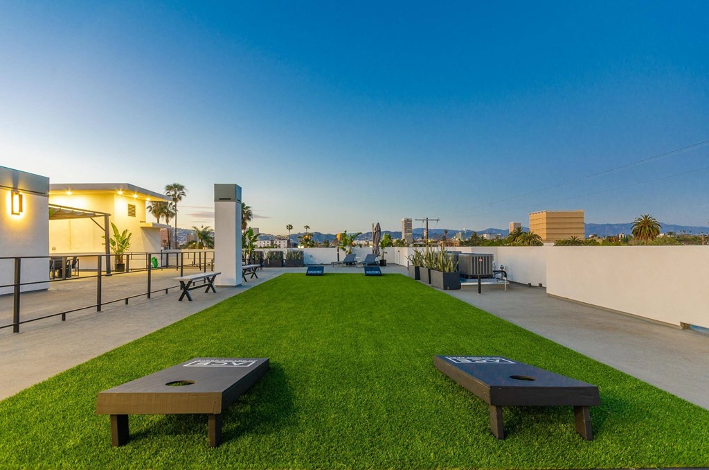 A rooftop deck with a lawn and two corn hole game wooden panels.