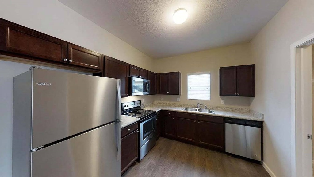 A kitchen with a stainless steel refrigerator and dark brown cabinets.