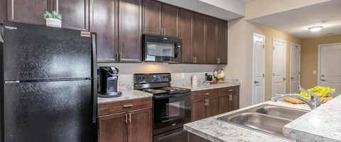 A black refrigerator is in a kitchen with brown cabinets.
