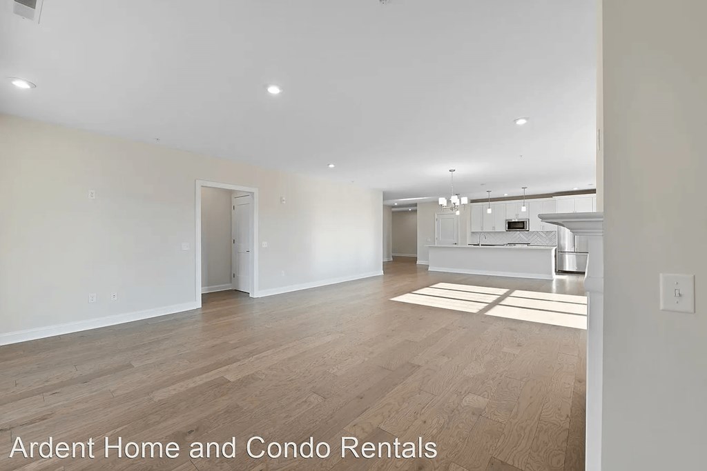 an empty living room with a kitchen in the background