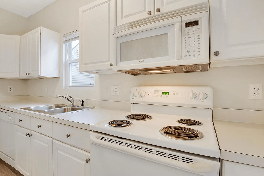 A white kitchen with a stove, sink, and cabinets.
