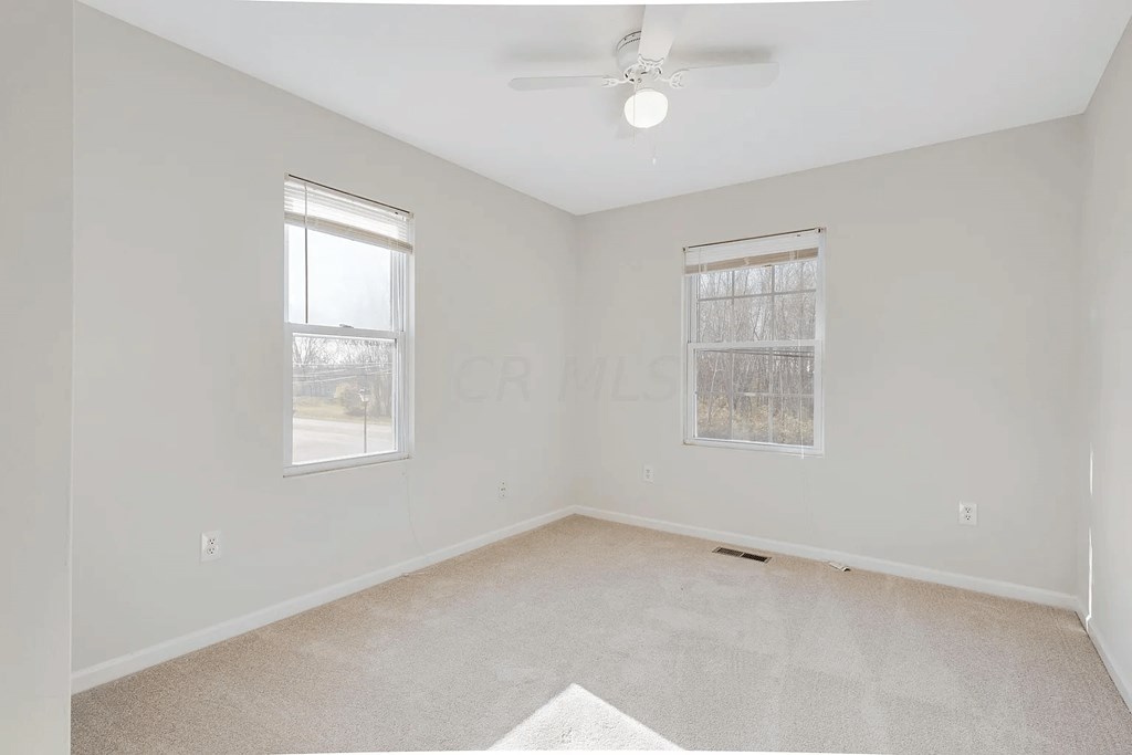 an empty living room with two windows and a ceiling fan