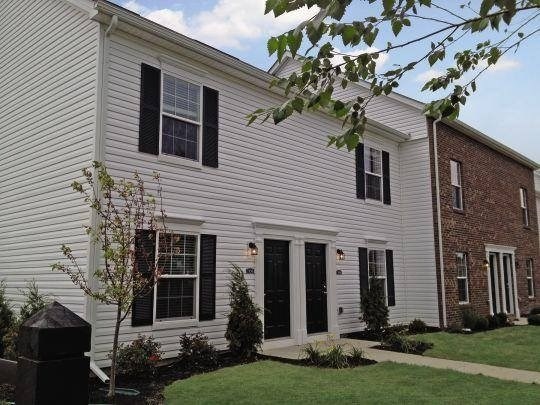 A white house with black shutters and a brick building next to it.