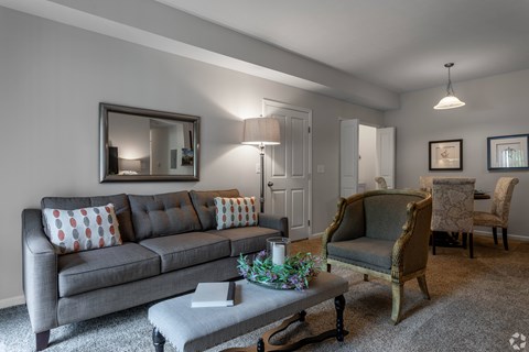 A grey couch with red and white pillows sits in a living room with a grey coffee table in front of it.