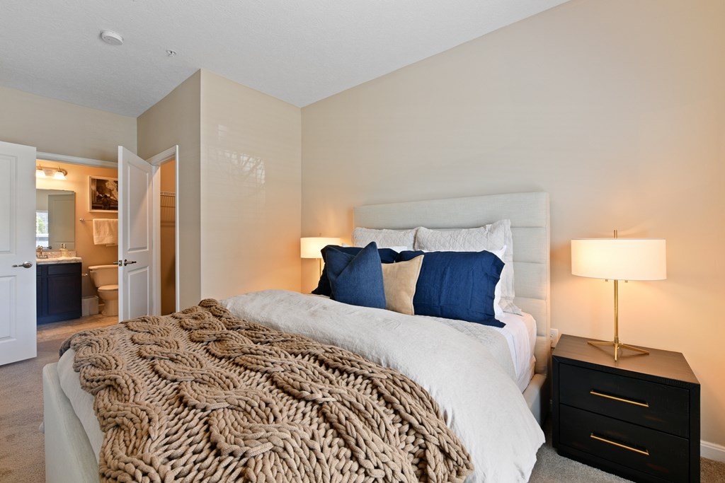 A bedroom with a large bed and a lamp on a nightstand.