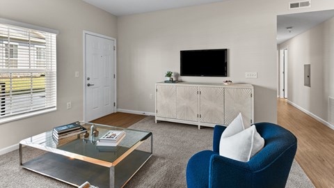 A living room with a blue armchair, a glass coffee table, and a television on a cabinet.
