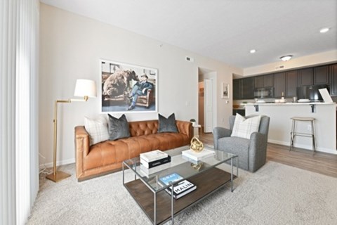 A living room with a brown leather couch, a glass coffee table, and a painting on the wall.