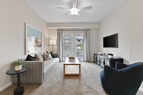 A living room with a grey couch, a blue chair, and a television on the wall.