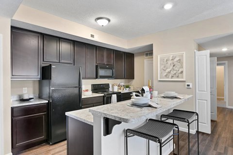 A kitchen with a black refrigerator and brown cabinets.