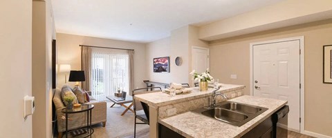 A kitchen with a sink and a counter with a table and chairs in the living room.