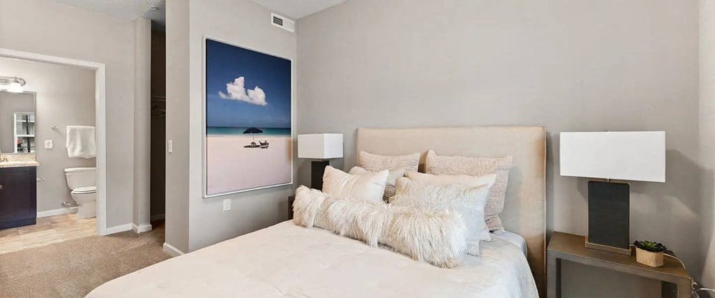 A bedroom with a large bed and a painting of a beach scene on the wall.