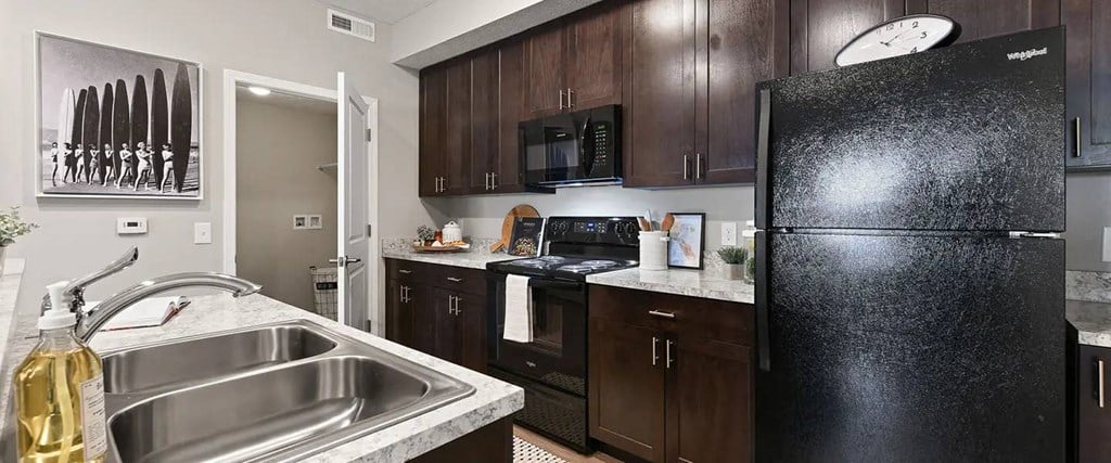 A black refrigerator is in a kitchen with a stove and sink.
