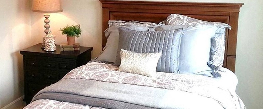 A bed with a grey comforter and a wooden headboard.