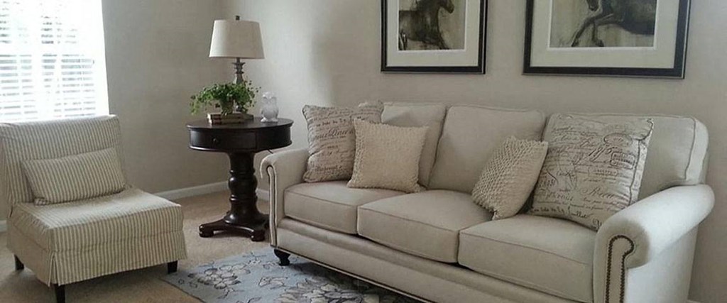 A living room with a white couch, a chair, and a table with a lamp and a plant on it.