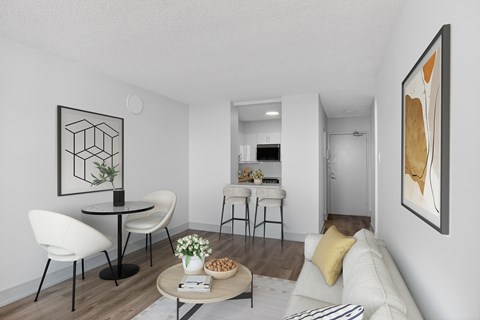 A modern living room with a white sofa, a round table with chairs, and a painting on the wall.