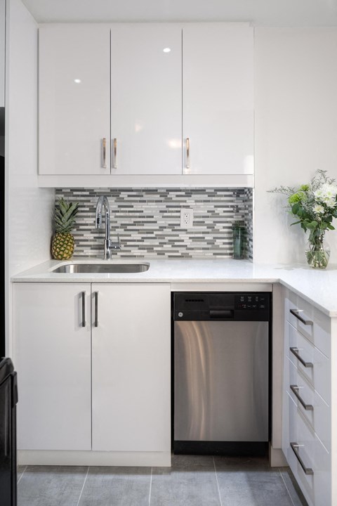 A modern kitchen with a stainless steel dishwasher and white cabinets.