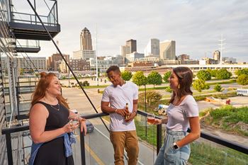 Three people are standing on a balcony with a city skyline in the background.at Linc, Des Moines, IA 50309  