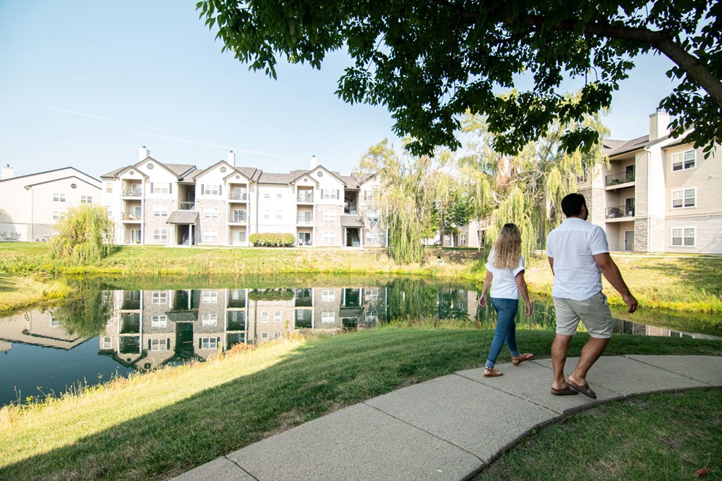 A man and a woman are walking along a path by a pond in front of apartment buildings.at 92West, Iowa  
