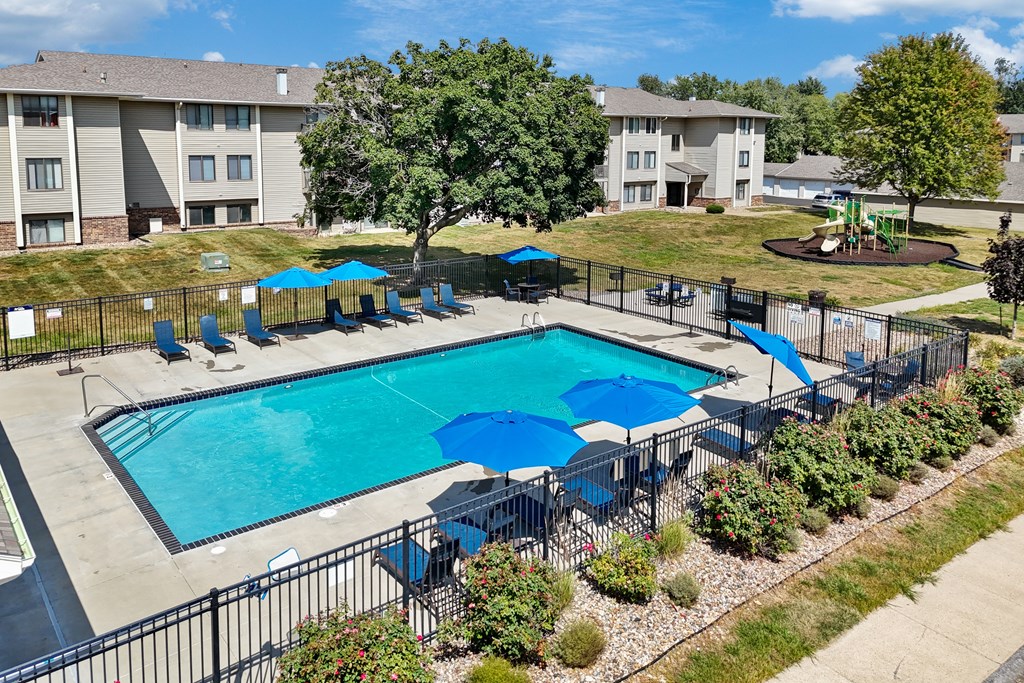 A swimming pool surrounded by a black fence and blue umbrellas.