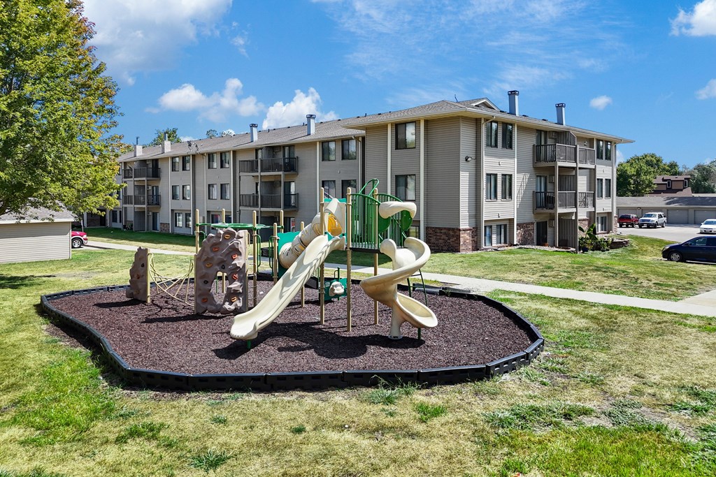 A playground with a slide and a merry-go-round in front of apartment buildings.
