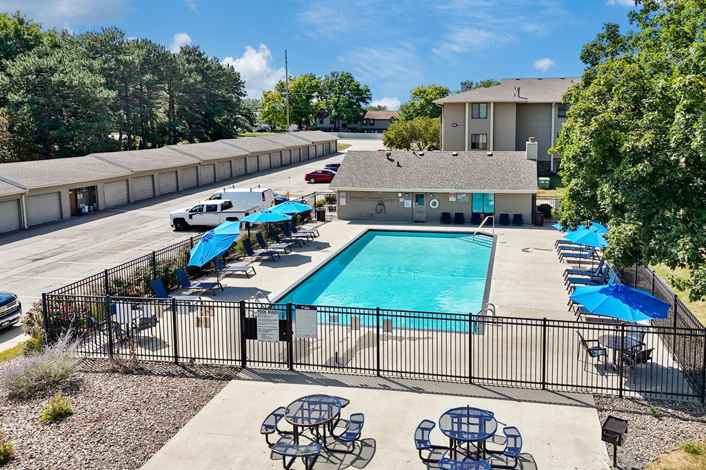 A pool surrounded by a black fence with blue umbrellas and chairs.