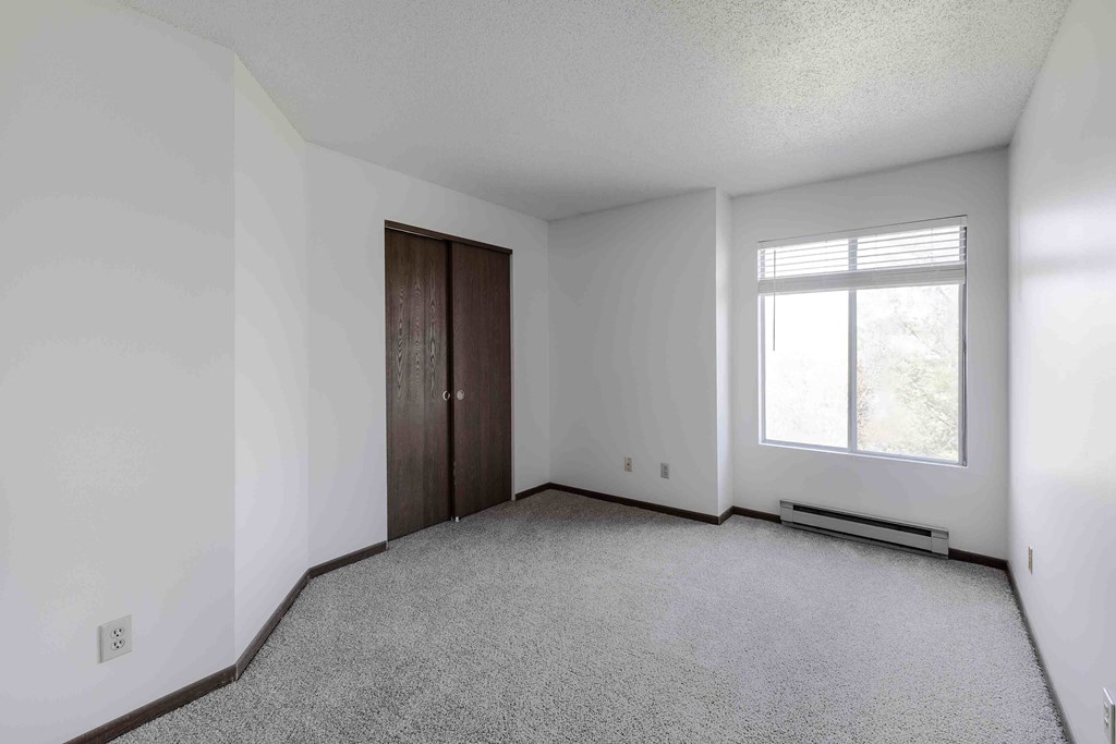 A room with a carpeted floor, a window with blinds, and a door.