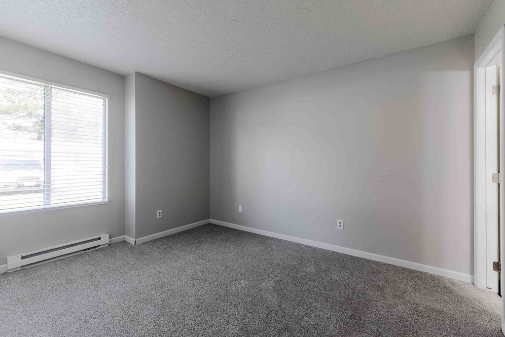 A room with a carpeted floor and a window with blinds.