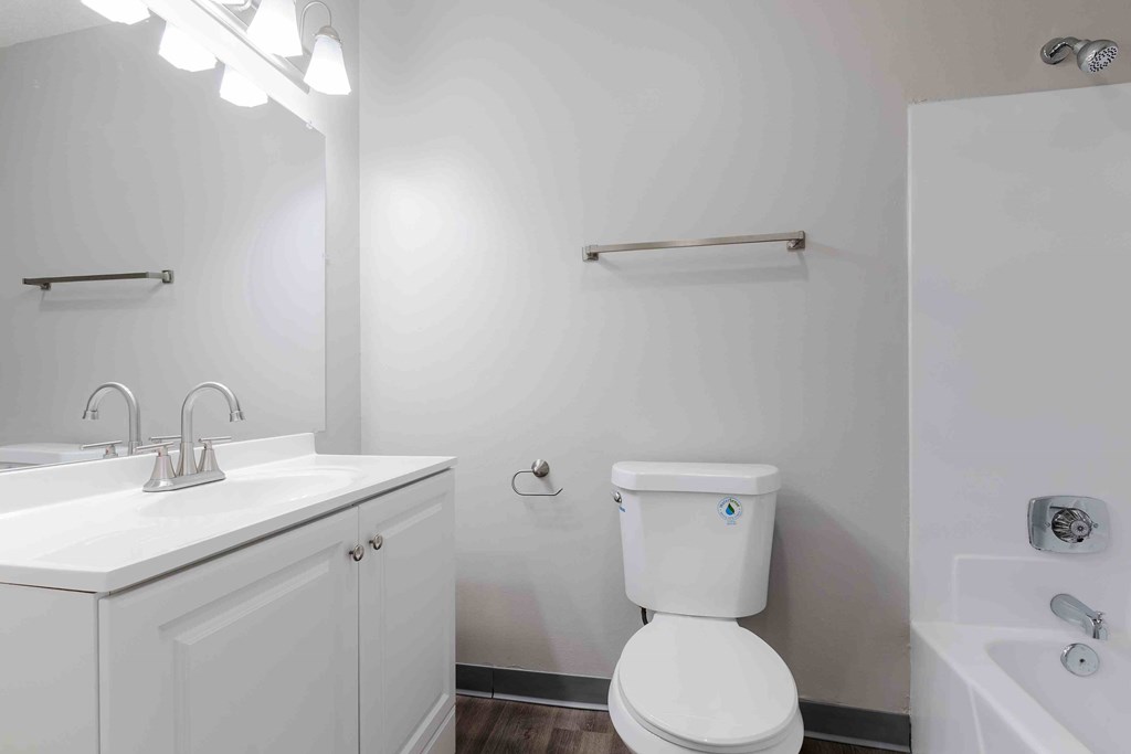 A white toilet with a blue sticker on the lid is in a bathroom with a white sink and a white cabinet.