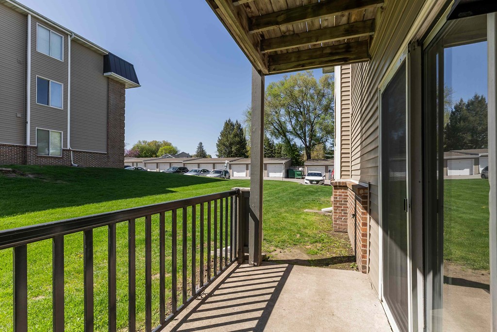 A balcony with a black railing and a view of a grassy area and other buildings.