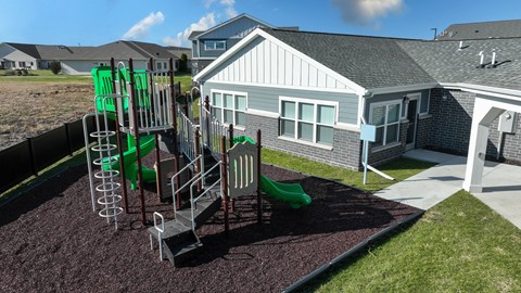 A playground with a green slide and a grey house in the background.
