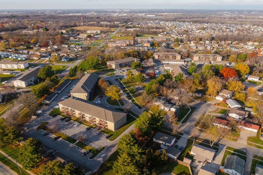 A large building with a parking lot in front of it is surrounded by trees and other buildings. at Rosemont Place Apartments, Des Moines, Iowa