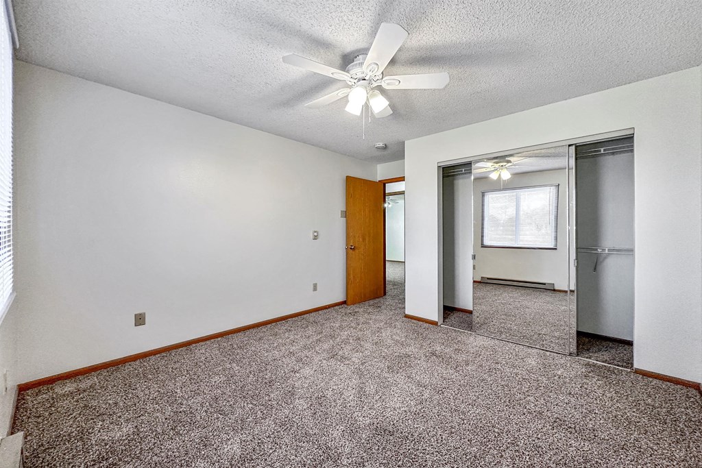 an empty living room with a ceiling fan and a refrigerator at Somerset Apartments, Des Moines