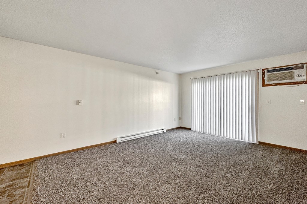 A room with a carpeted floor and a window with blinds at Somerset Apartments, Des Moines, Iowa