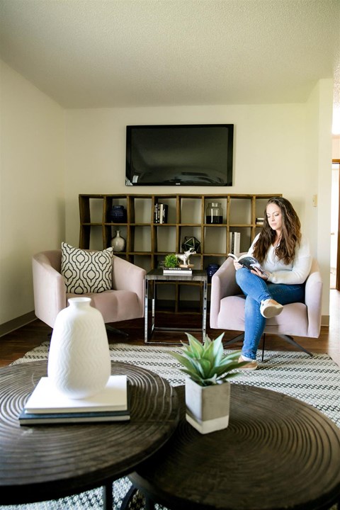 A woman is sitting on a chair in a living room with a TV mounted on the wall.